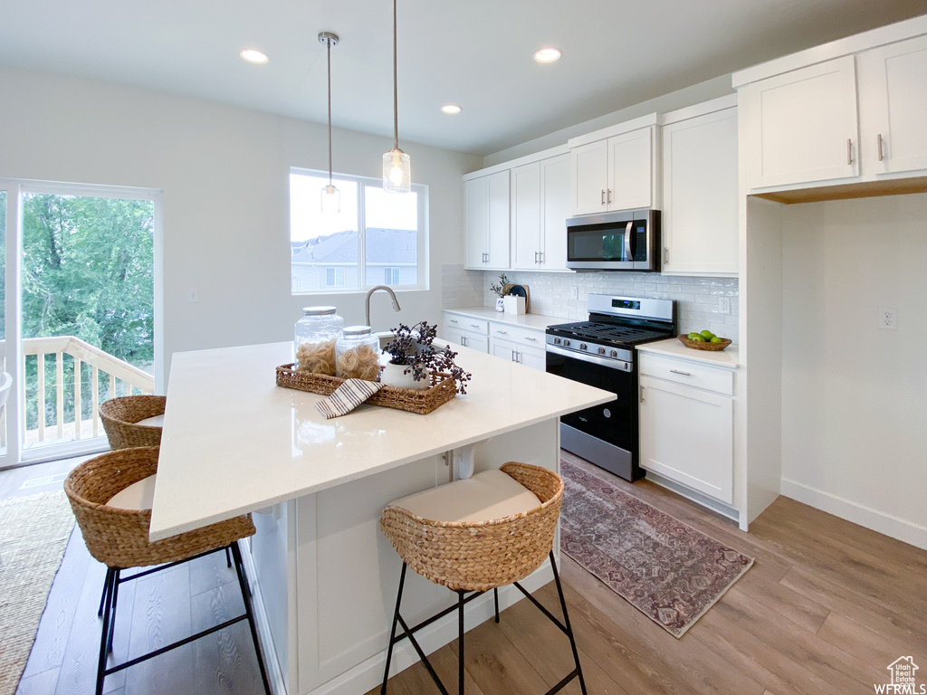 Kitchen featuring stainless steel appliances, light wood-style floors, decorative backsplash, a breakfast bar, and white cabinets
