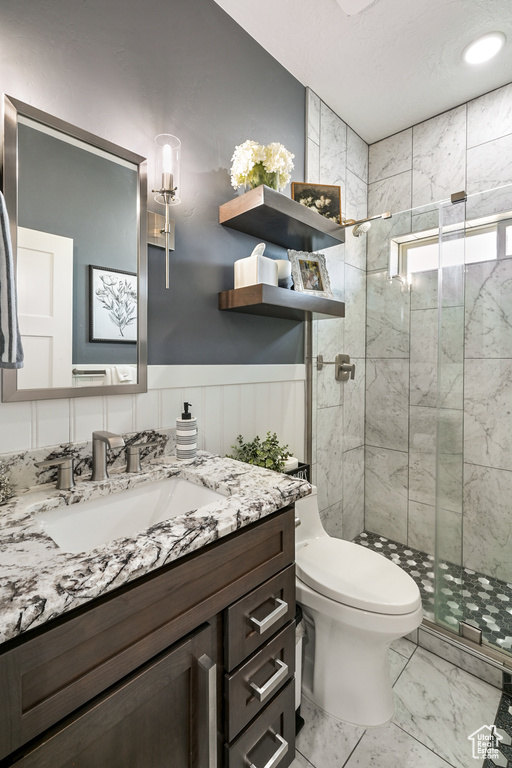 Full bath featuring vanity, a shower stall, marble finish flooring, and wainscoting