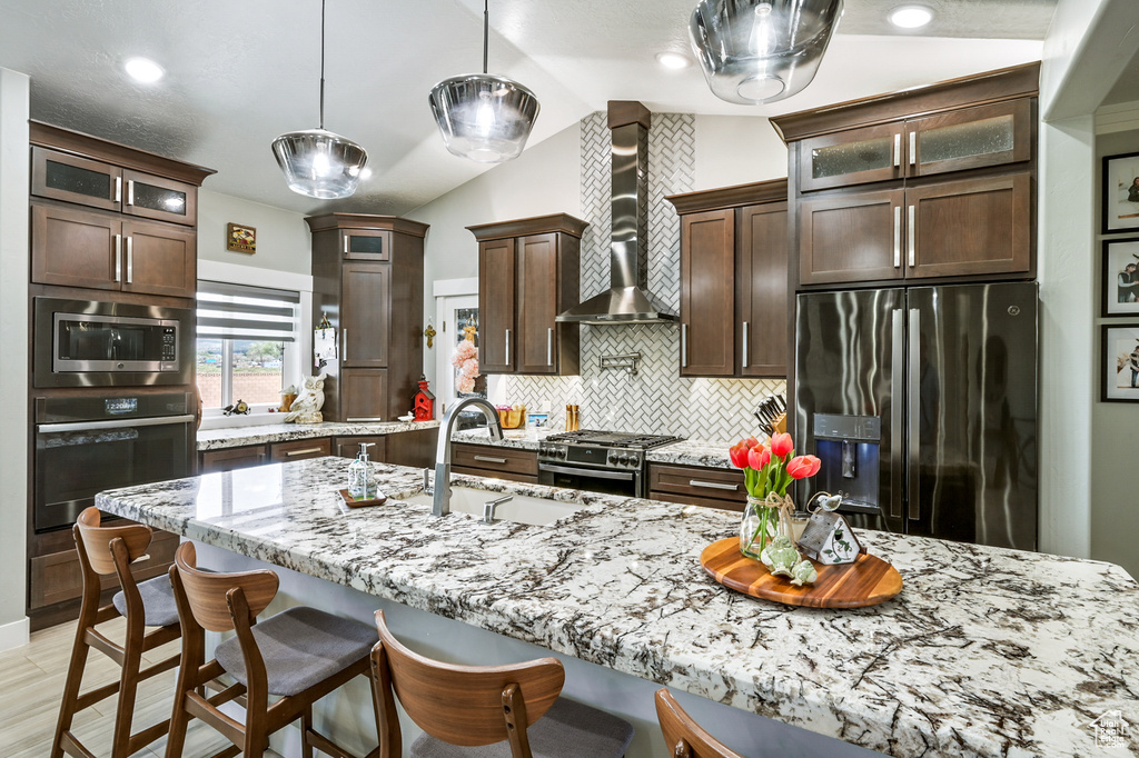 Kitchen with stainless steel appliances, wall chimney exhaust hood, lofted ceiling, backsplash, and glass insert cabinets