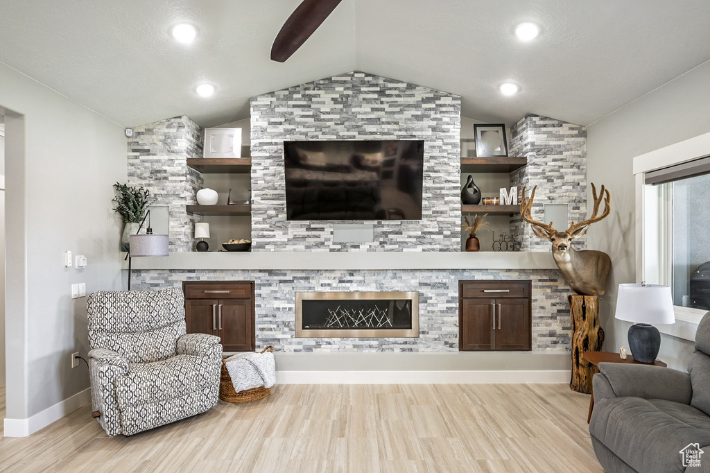 Living room with vaulted ceiling, light wood finished floors, a ceiling fan, and a glass covered fireplace