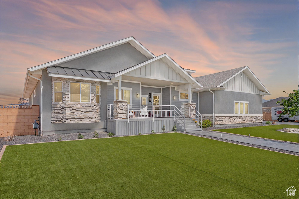 Craftsman house featuring stone siding, covered porch, a front yard, and a standing seam roof