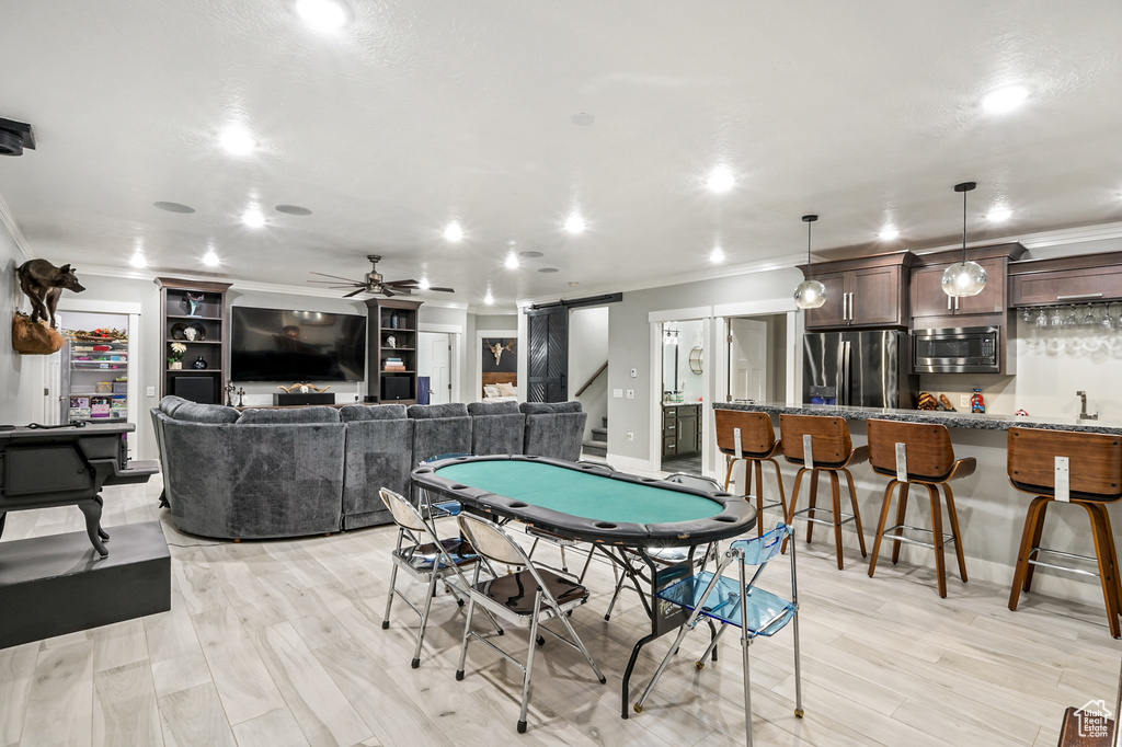 Rec room featuring a barn door, ornamental molding, wet bar, ceiling fan, and recessed lighting