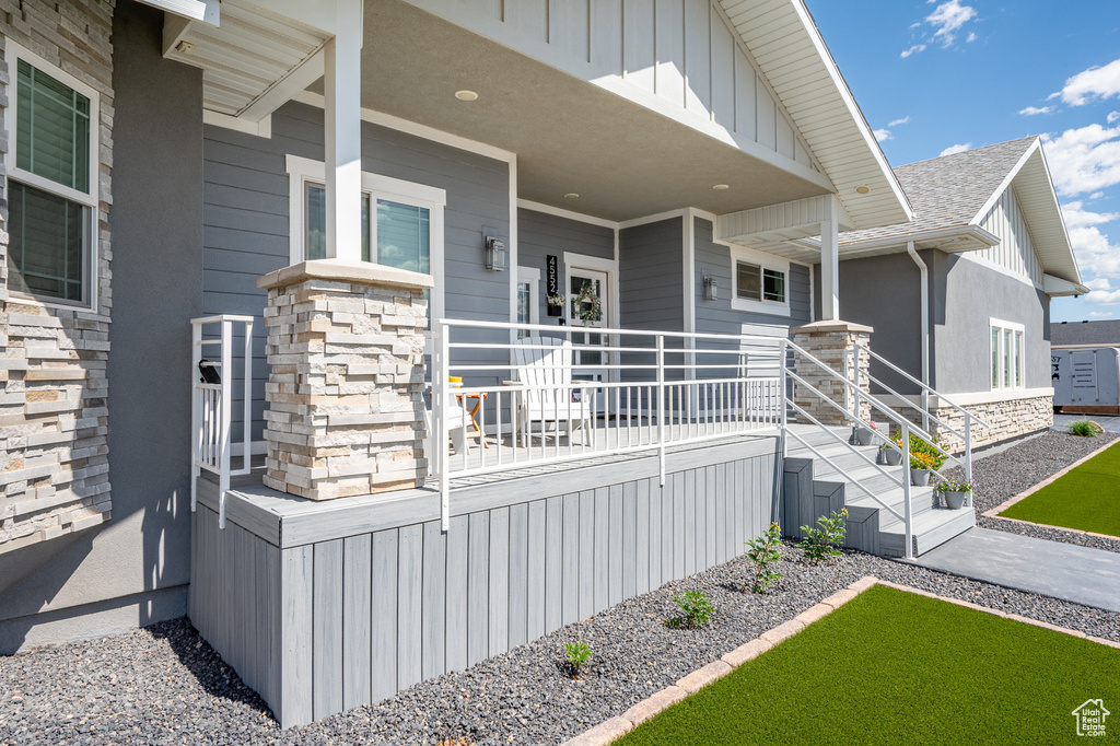 View of exterior entry with stone siding, covered porch, a shingled roof, and board and batten siding