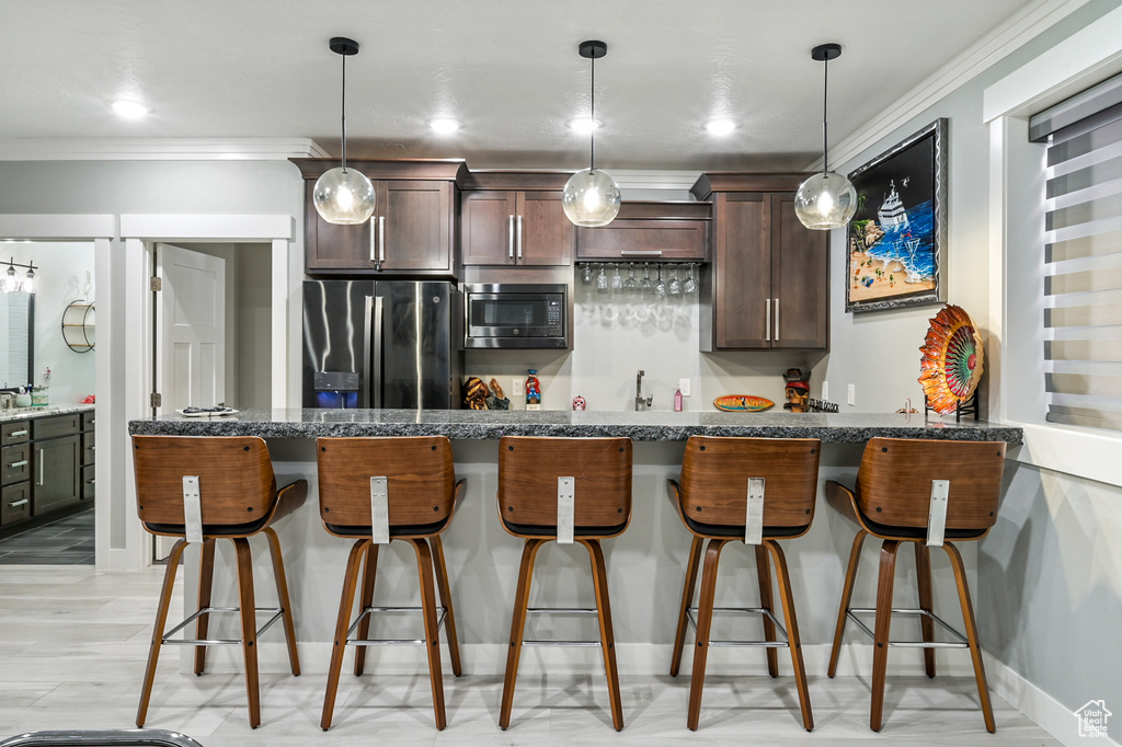 Kitchen featuring stainless steel fridge with ice dispenser, built in microwave, crown molding, dark brown cabinetry, and a kitchen breakfast bar