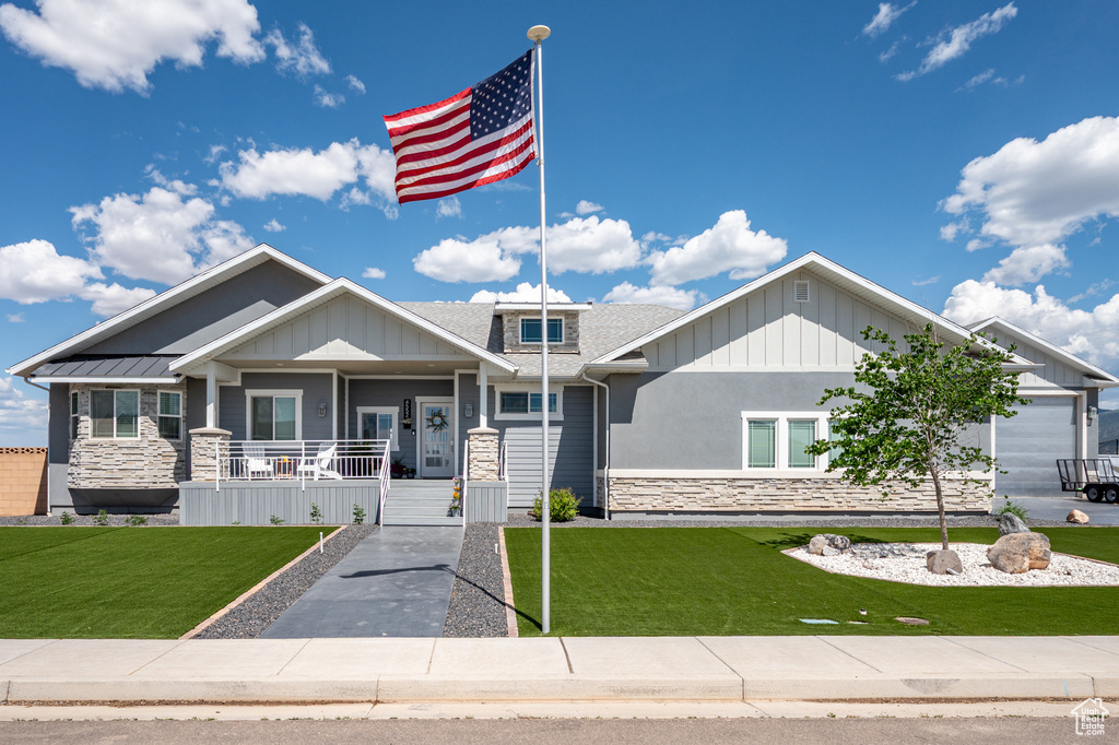 Craftsman-style house featuring stone siding, covered porch, a front lawn, and board and batten siding