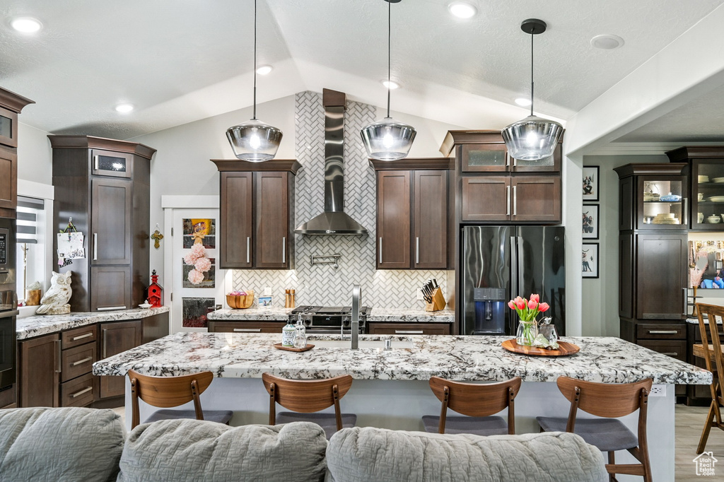 Kitchen with stainless steel fridge with ice dispenser, wall chimney exhaust hood, open floor plan, a breakfast bar area, and lofted ceiling