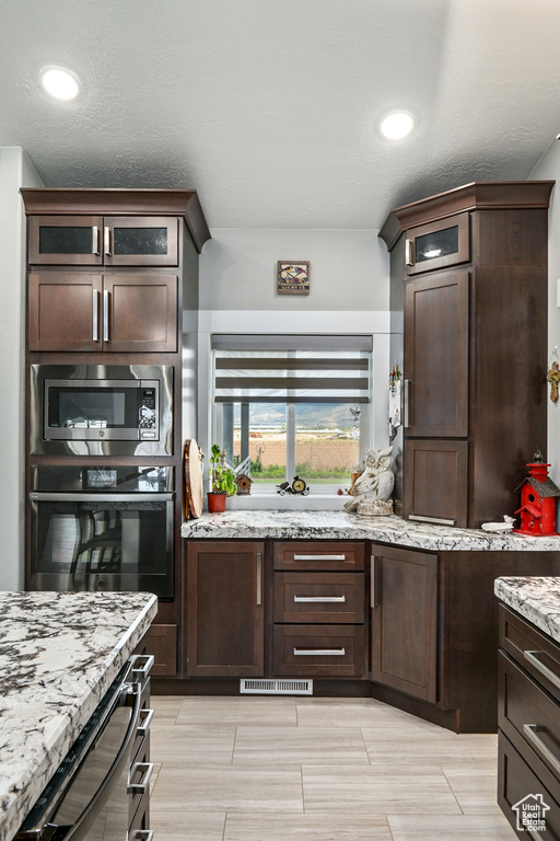 Kitchen with stainless steel appliances, dark brown cabinetry, and light stone counters