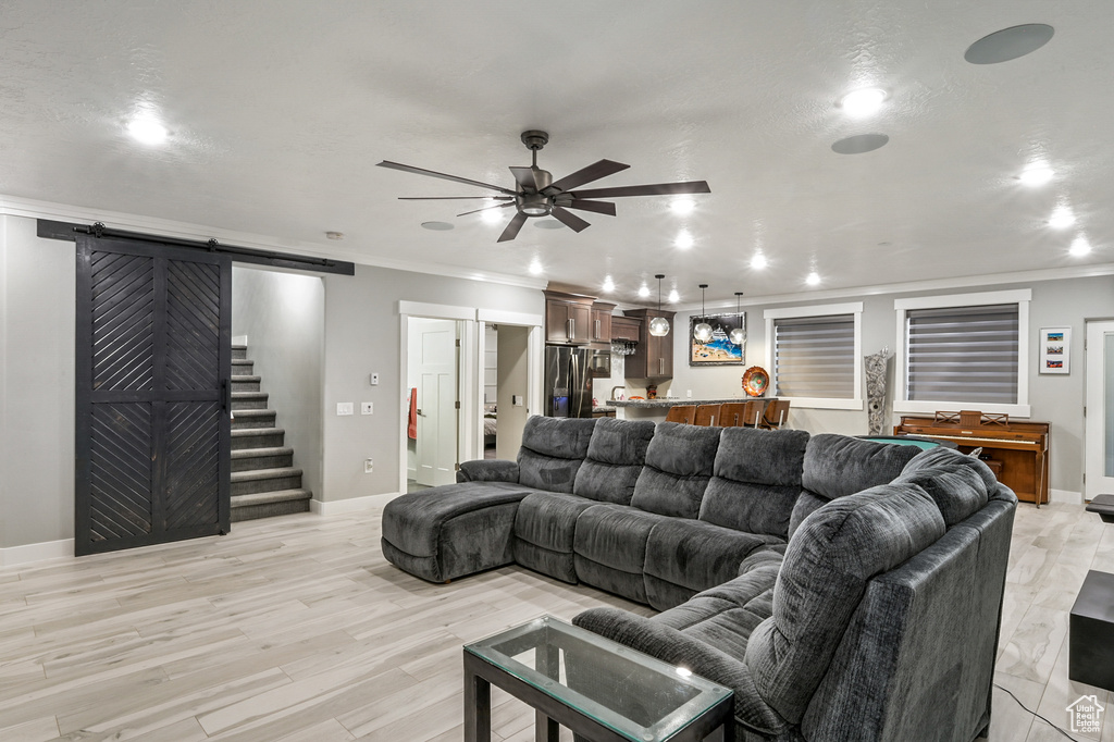 Living room with a barn door, crown molding, ceiling fan, light wood-style floors, and recessed lighting