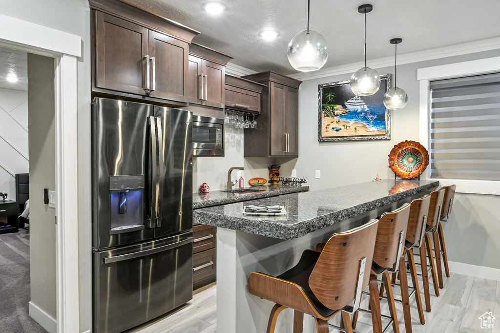 Kitchen with appliances with stainless steel finishes, dark brown cabinetry, a breakfast bar area, light wood finished floors, and hanging light fixtures