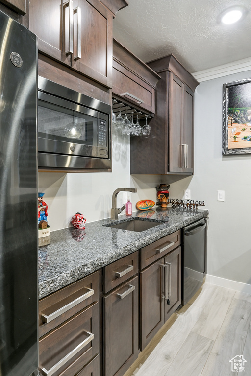 Kitchen with appliances with stainless steel finishes, dark stone countertops, dark brown cabinets, a textured ceiling, and ornamental molding