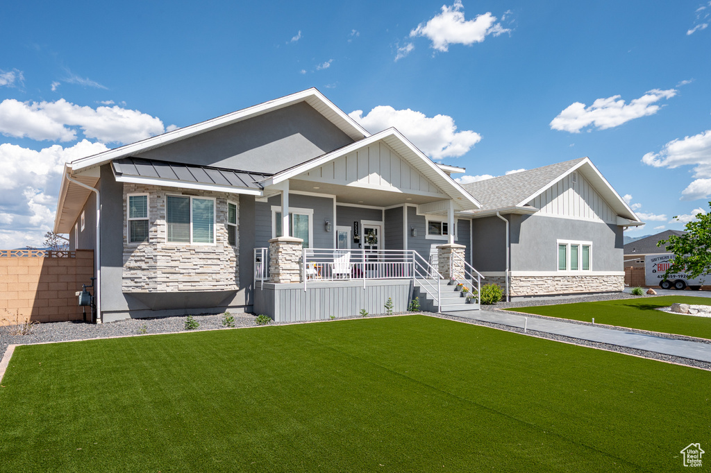 Craftsman-style home with stone siding, covered porch, a front lawn, and a standing seam roof