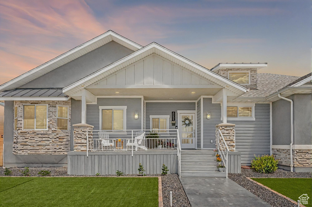 View of front of house featuring stone siding, a porch, a front lawn, and a standing seam roof