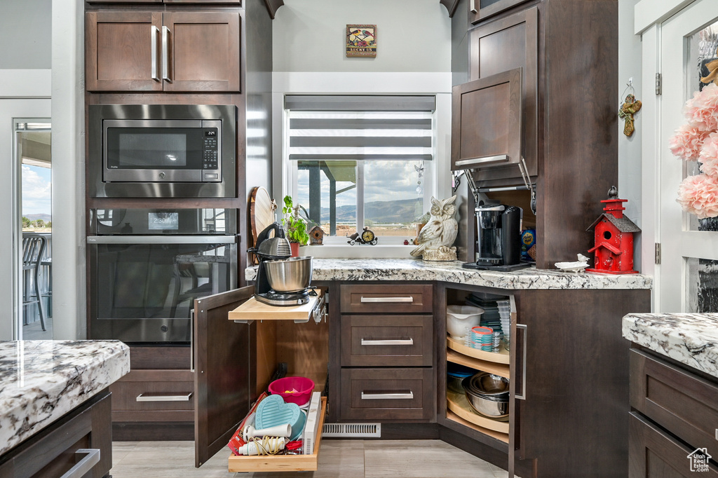 Kitchen featuring oven, stainless steel microwave, dark brown cabinetry, and light stone counters