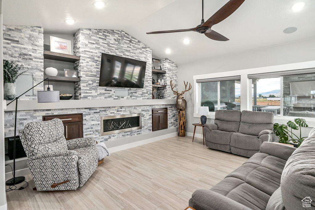 Living area with ceiling fan, a stone fireplace, lofted ceiling, wood finished floors, and recessed lighting