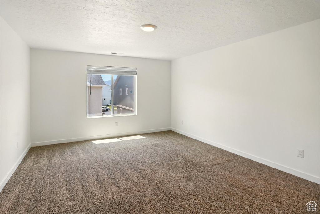 Carpeted spare room featuring baseboards and a textured ceiling