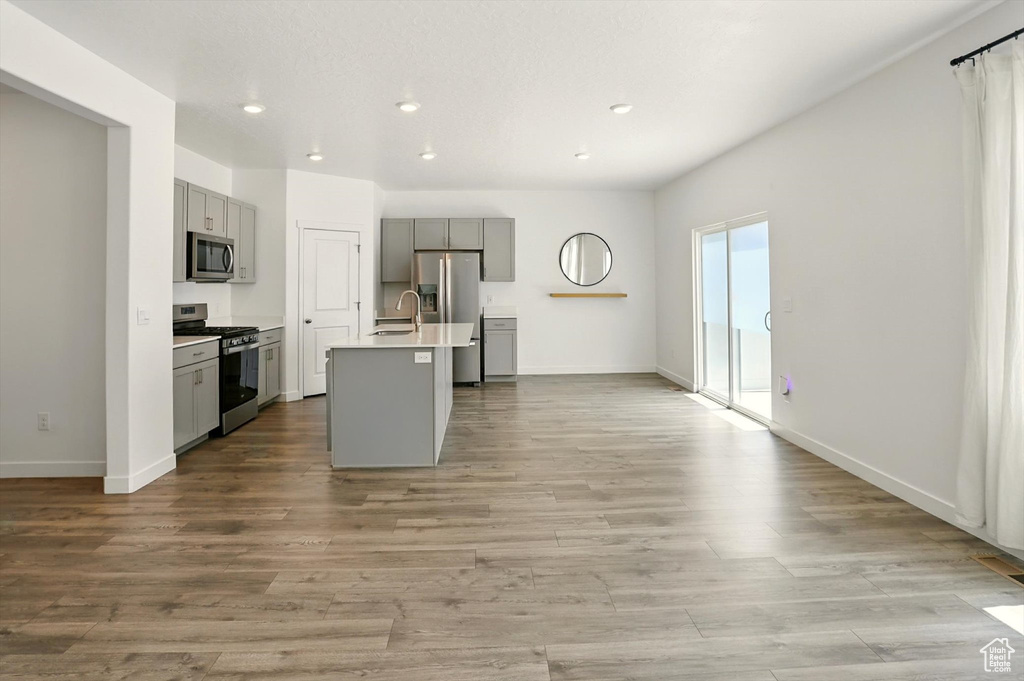 Kitchen with stainless steel appliances, gray cabinetry, light countertops, recessed lighting, and a center island with sink