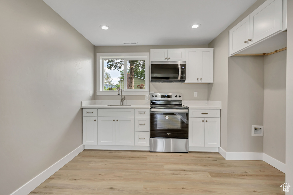 Kitchen with appliances with stainless steel finishes, light countertops, white cabinetry, light wood-type flooring, and recessed lighting