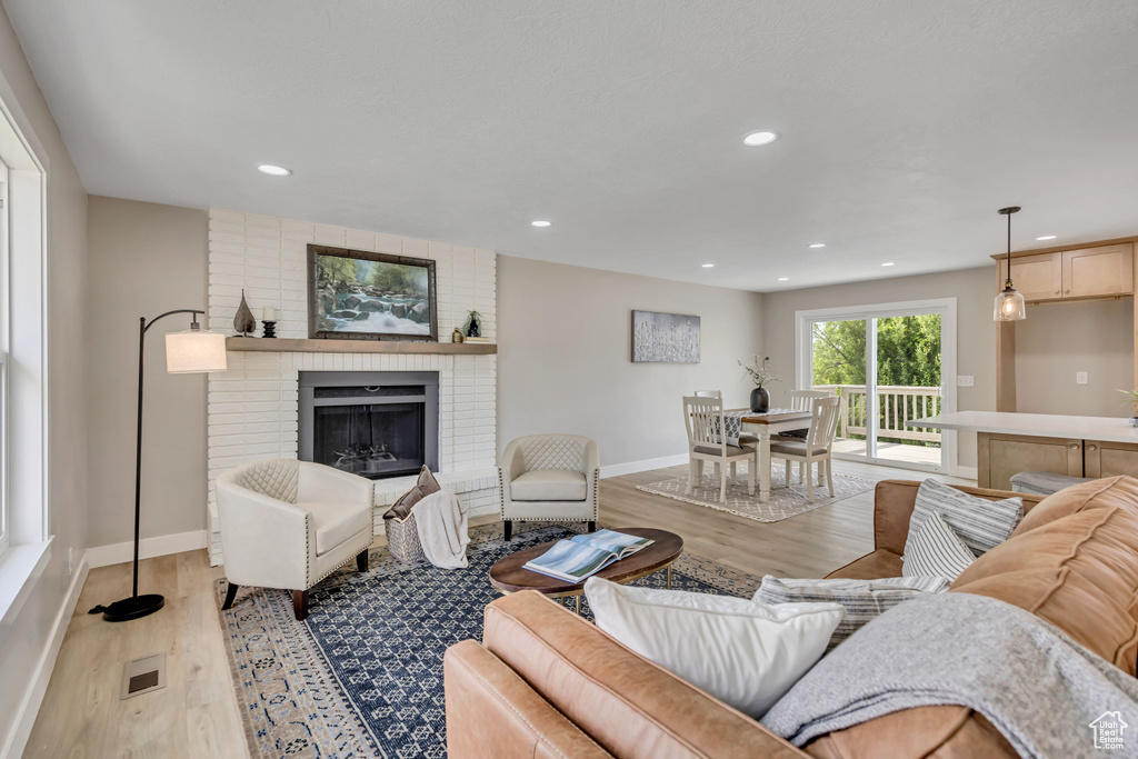 Living room featuring light wood-type flooring, recessed lighting, and a brick fireplace
