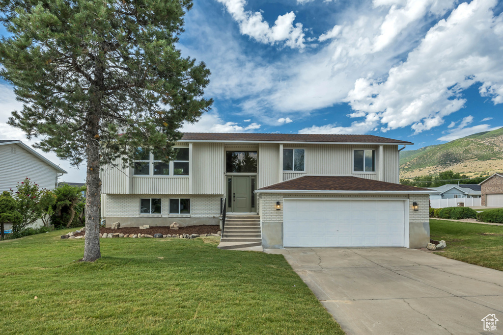 Bi-level home featuring driveway, a mountain view, a front yard, and a garage