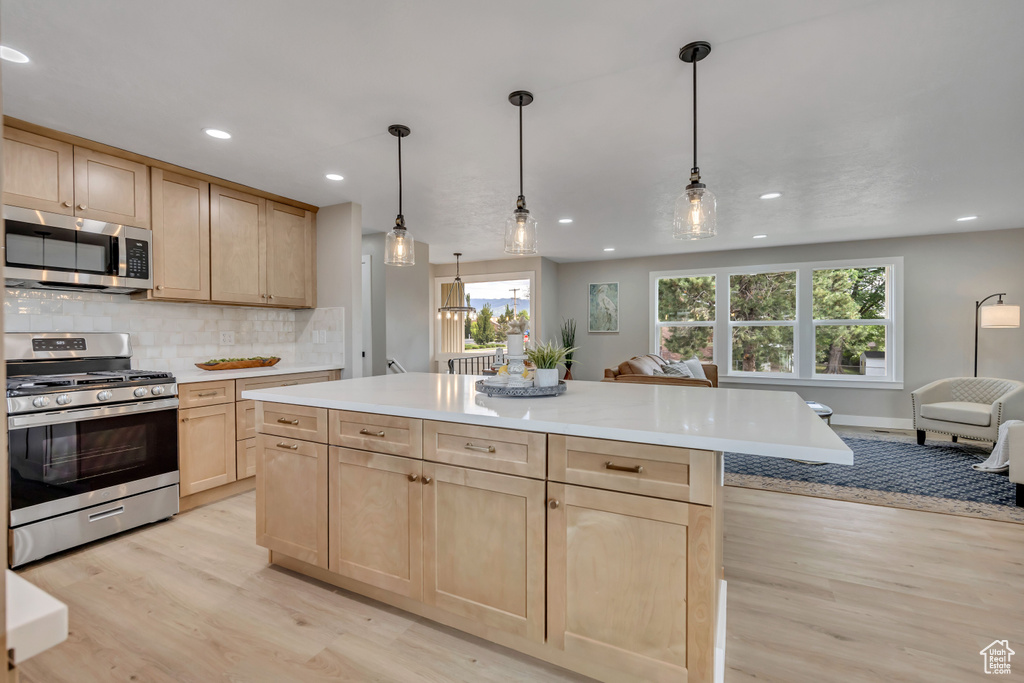Kitchen with stainless steel appliances, light brown cabinets, open floor plan, light wood finished floors, and light countertops