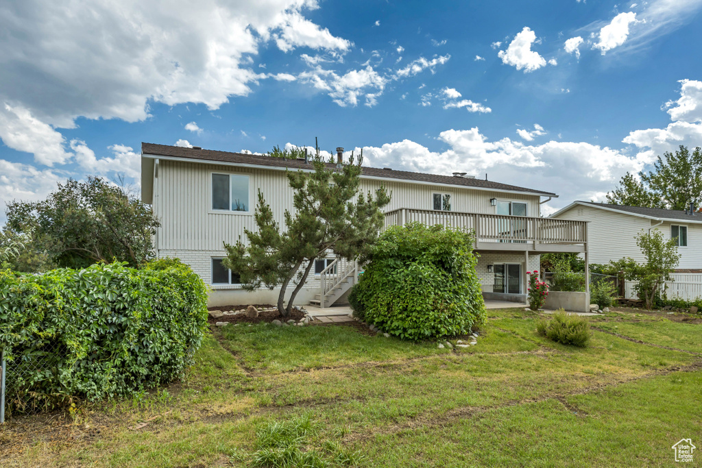 Rear view of property with a wooden deck, stairs, and a lawn