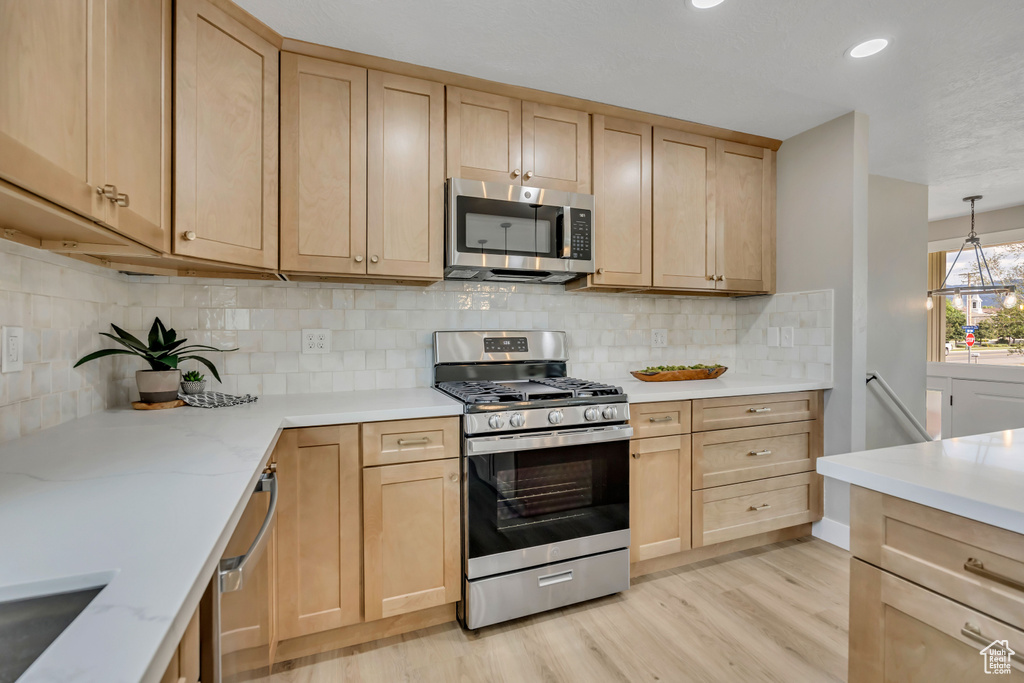 Kitchen featuring stainless steel appliances, light brown cabinets, light wood finished floors, tasteful backsplash, and light stone counters