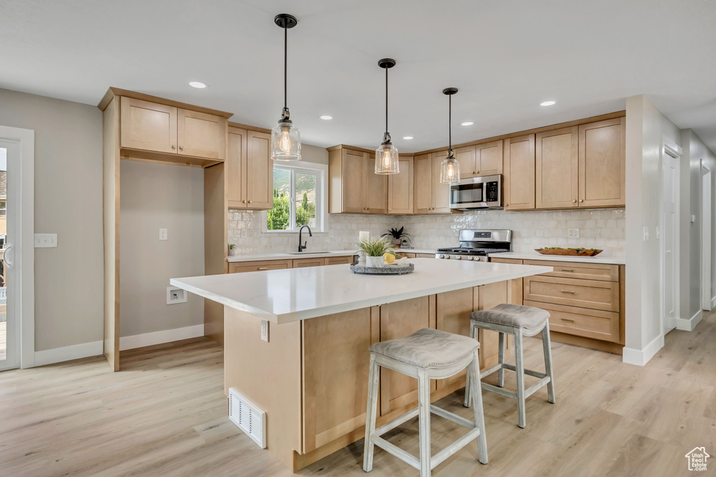 Kitchen with appliances with stainless steel finishes, light wood-style flooring, backsplash, light countertops, and light brown cabinets