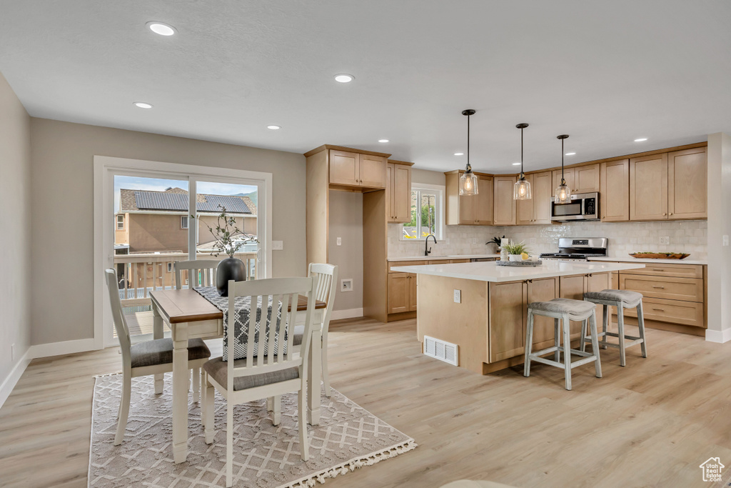 Kitchen with stainless steel appliances, a kitchen island, decorative backsplash, light countertops, and light wood-type flooring