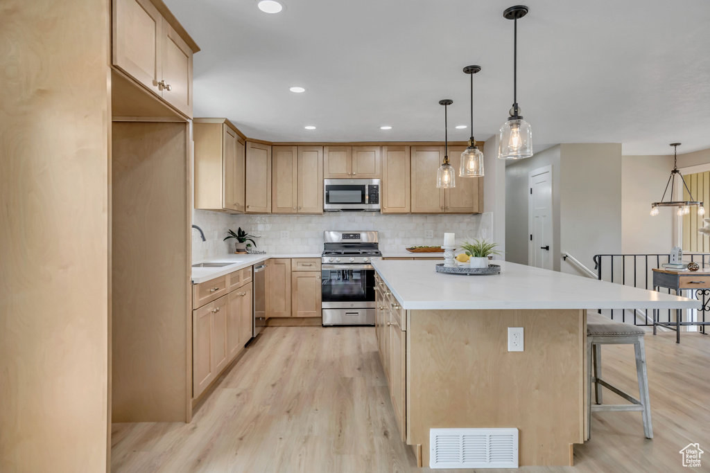 Kitchen featuring appliances with stainless steel finishes, light brown cabinets, light wood-style floors, a kitchen island, and recessed lighting