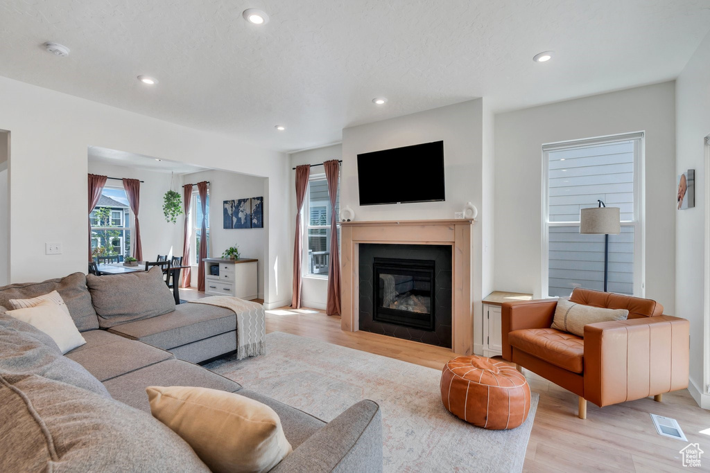 Living area featuring light wood-style floors, recessed lighting, and a glass covered fireplace