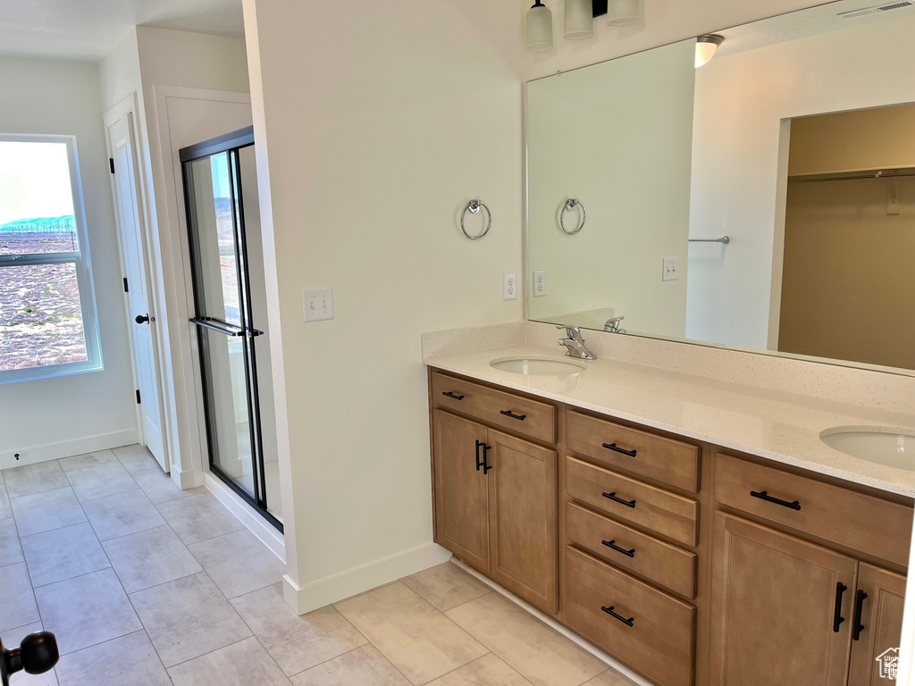 Full bath with a shower stall, double vanity, tile patterned floors, and a walk in closet