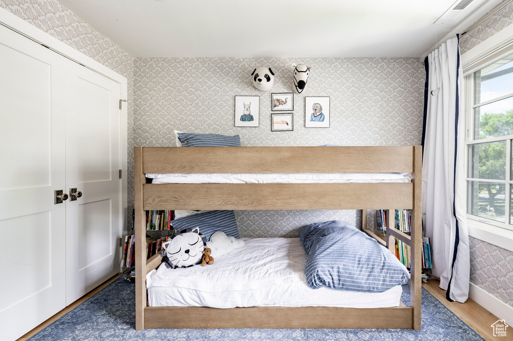 Bedroom with wallpapered walls, wood finished floors, and a closet