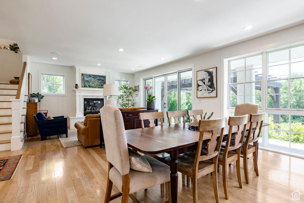 Dining space with light wood finished floors, stairway, a glass covered fireplace, and recessed lighting