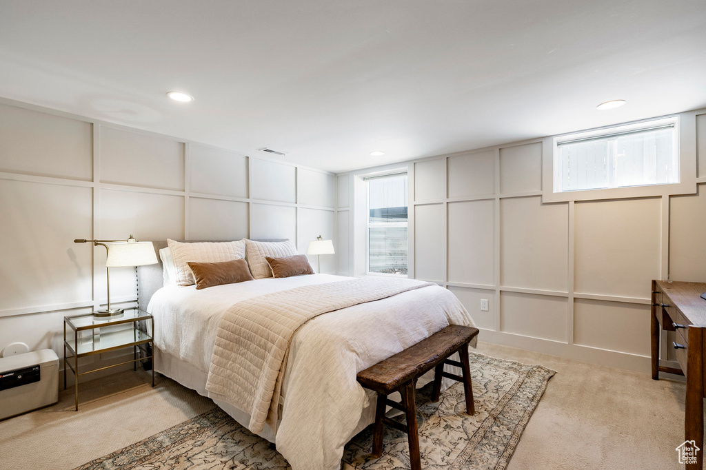Bedroom featuring a decorative wall, light colored carpet, and multiple windows