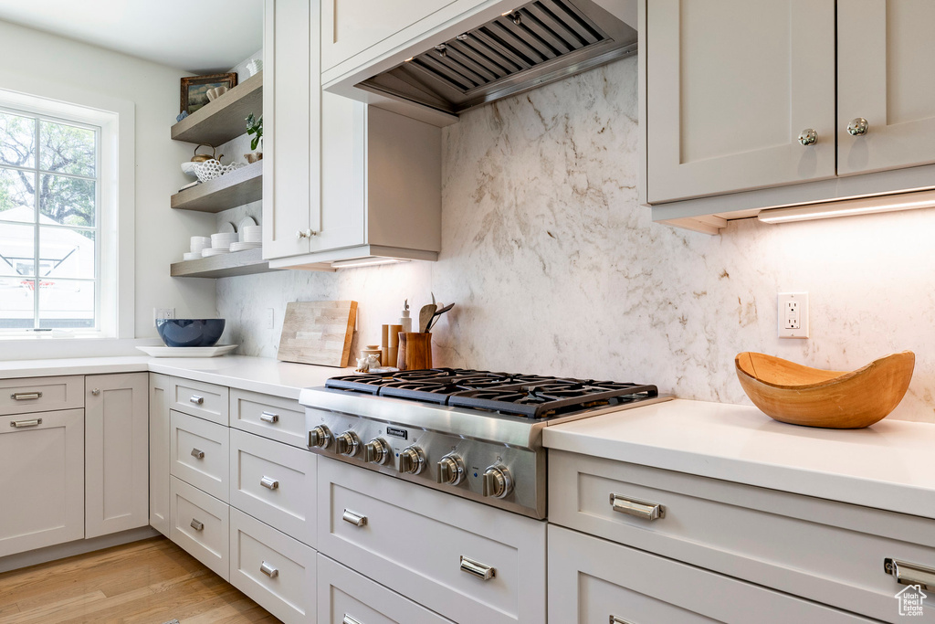 Kitchen with custom range hood, open shelves, stainless steel gas cooktop, and tasteful backsplash
