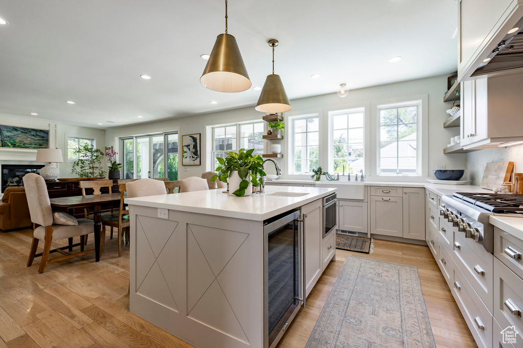 Kitchen featuring stainless steel gas cooktop, beverage cooler, open shelves, light countertops, and an island with sink