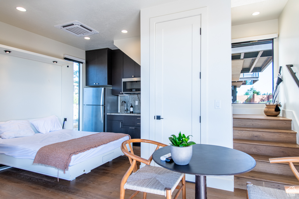 Bedroom with freestanding refrigerator, wood finished floors, recessed lighting, and bar with sink