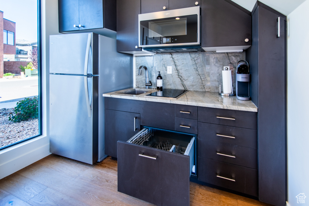 Kitchen featuring appliances with stainless steel finishes, light countertops, backsplash, light wood-style flooring, and modern cabinets