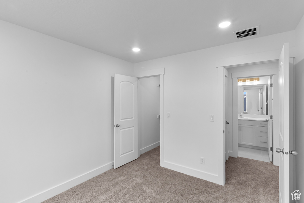 Unfurnished bedroom featuring carpet, recessed lighting, a walk in closet, and ensuite bath