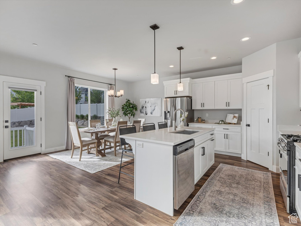 Kitchen with appliances with stainless steel finishes, a breakfast bar area, an island with sink, white cabinetry, and dark wood-style flooring