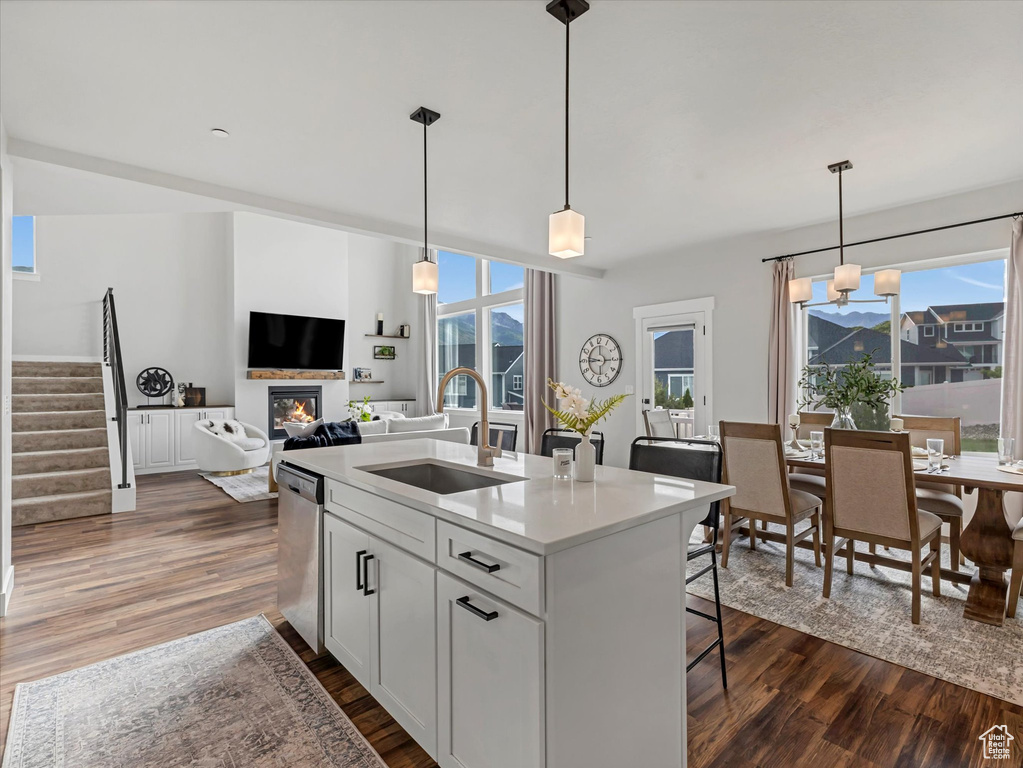 Kitchen with stainless steel dishwasher, a glass covered fireplace, dark wood-style floors, a breakfast bar, and white cabinets