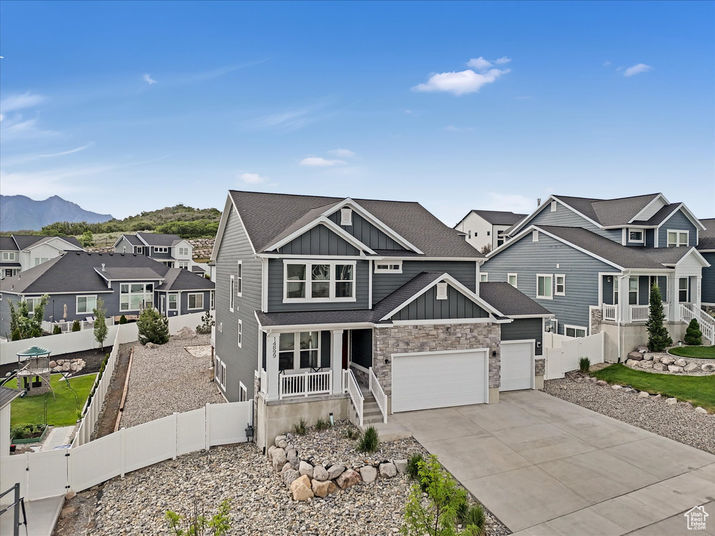 View of front of house with board and batten siding, a porch, a residential view, concrete driveway, and a mountain view