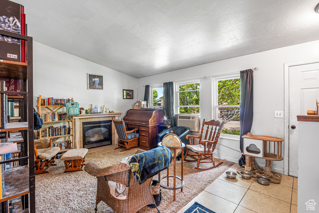 Living room featuring lofted ceiling, cooling unit, tile patterned floors, a textured ceiling, and a glass covered fireplace