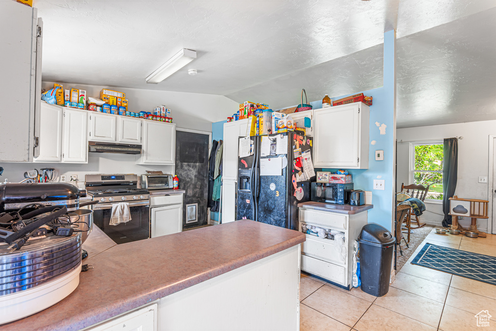 Kitchen featuring stainless steel range with gas cooktop, vaulted ceiling, light tile patterned flooring, under cabinet range hood, and white cabinets