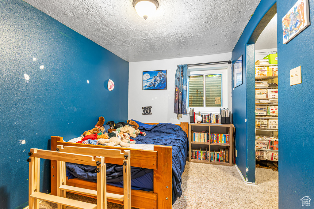 Bedroom with a textured ceiling, carpet flooring, a textured wall, and arched walkways