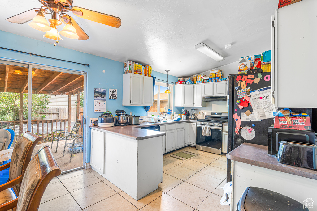 Kitchen with stainless steel gas range oven, under cabinet range hood, a peninsula, and light tile patterned floors