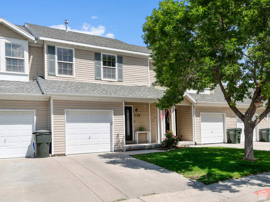Multi unit property featuring a porch, an attached garage, driveway, a front yard, and a shingled roof