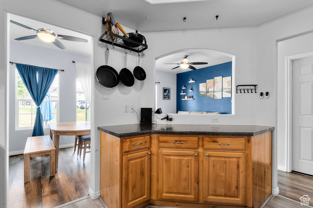 Kitchen featuring a ceiling fan, arched walkways, wood finished floors, brown cabinets, and dark stone countertops