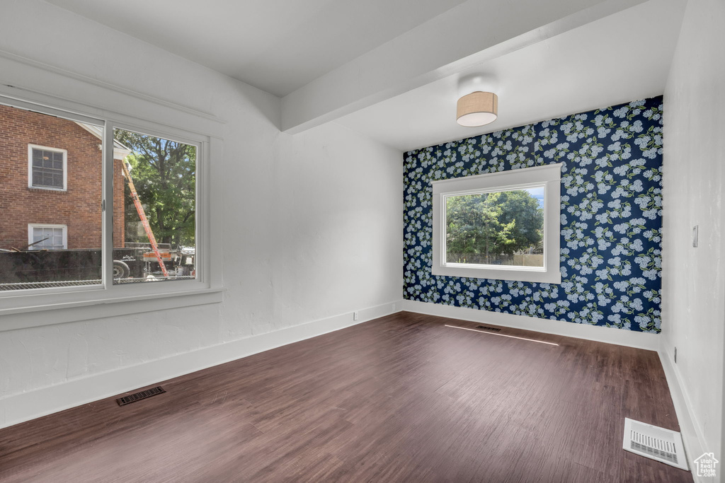 Unfurnished room with wallpapered walls, plenty of natural light, and dark wood-type flooring
