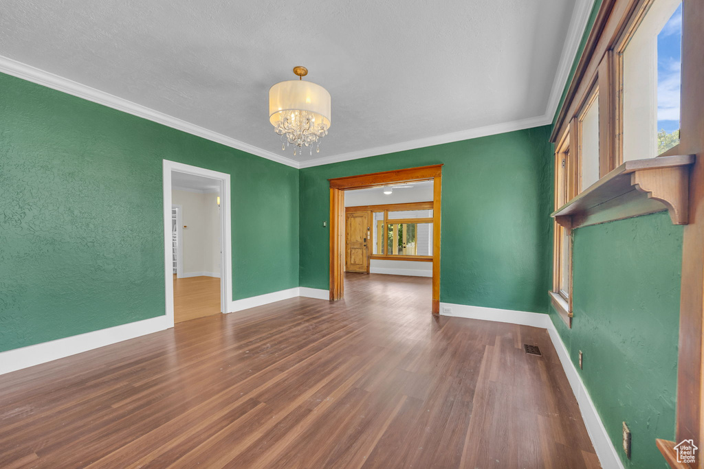 Empty room with a chandelier, wood finished floors, crown molding, and a textured wall